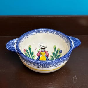 May include: A white ceramic mug with a black handle and the text "But First, Coffee" in a bold, black font. The mug is set against a blurred background, suggesting a cozy setting.