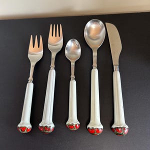 Puede incluir: Conjunto de cinco cubiertos vintage con mangos de cerámica blanca y detalles florales rojos. El conjunto incluye dos tenedores, dos cucharas y un cuchillo para mantequilla.