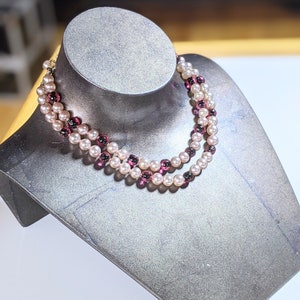 Può includere: Una collana a doppio filo con perline rosa e viola. La collana è esposta su un manichino grigio.