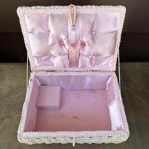 May include: White wicker sewing box with a pink satin lining and a padded lid. The box has a hinged lid and a small compartment inside.