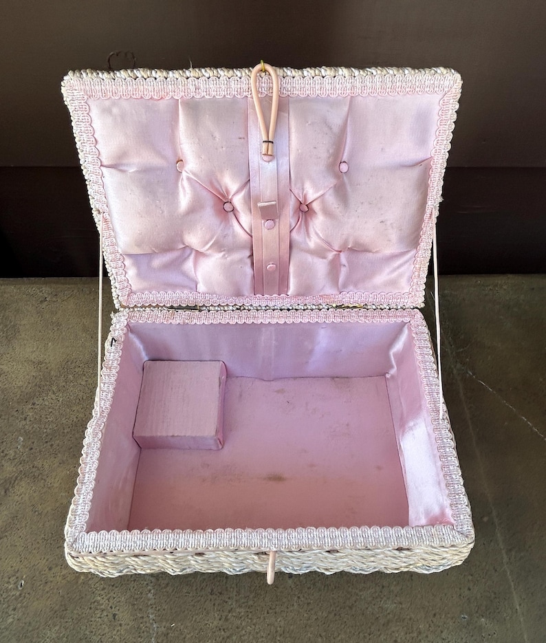 May include: White wicker sewing box with a pink satin lining and a padded lid. The box has a hinged lid and a small compartment inside.