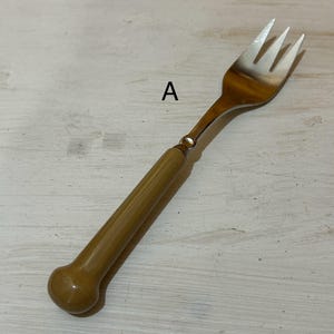 May include: A silver fork with a brown plastic handle. The handle is rounded at the end.