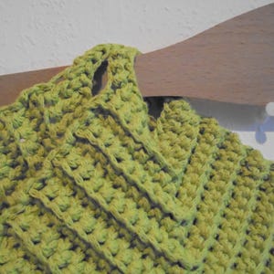 May include: Close-up of a lime green crocheted item, possibly a garment or accessory. The textured stitch pattern is visible, with a repeating geometric design. The item is hanging on a wooden hanger.