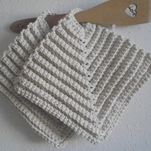 Pode incluir: Dois panos de cozinha de crochê brancos com formato quadrado e um padrão texturizado.