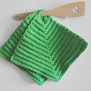 May include: Two green crocheted pot holders hanging on a wooden spoon with a heart-shaped design.