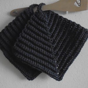May include: Two dark grey crocheted pot holders with a diamond pattern. The pot holders are hanging on a wooden spoon.