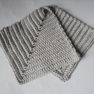 May include: Two grey crocheted pot holders with a textured design. One pot holder has a striped pattern.