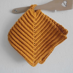 Puede incluir: Un posavasos de ganchillo de color amarillo mostaza con forma cuadrada y borde festoneado.