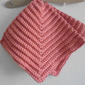 May include: Two pink crocheted squares with a chevron pattern. The squares are folded in half and are hanging from a wooden dowel.