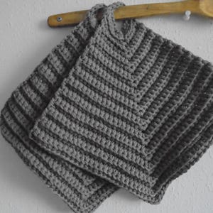 May include: Two grey crocheted pot holders with a striped pattern. The pot holders are hanging on a wooden spoon.