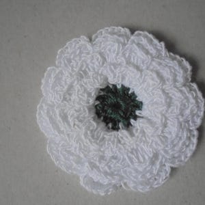 May include: A handmade, white crochet flower with a dark green center. The flower has multiple layers of petals, creating a textured, three-dimensional effect. This craft item could be used as an embellishment for clothing or accessories.