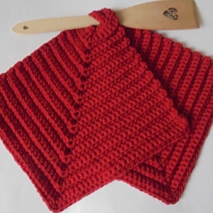 Puede incluir: Un juego de dos agarraderas rojas, hechas a mano, de ganchillo con un diseño acanalado. Una espátula de madera descansa sobre las agarraderas. Las agarraderas son cuadradas y tienen un lazo para colgar.