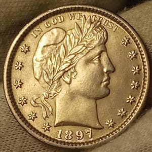 Może przedstawiać: Srebrna moneta z napisem "IN GOD WE TRUST" i rokiem "1897". Moneta przedstawia profil kobiety w wieńcu laurowym i jest otoczona gwiazdami.