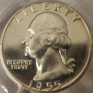 May include: A silver 1955 quarter coin. The coin shows a profile of George Washington, with the inscription "LIBERTY" at the top, and "IN GOD WE TRUST" and the date "1955" at the bottom. The coin has a shiny, reflective surface.