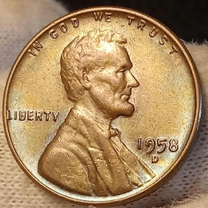 May include: A close-up of a copper-colored 1958 Lincoln penny. The coin features a profile of Abraham Lincoln, the word "LIBERTY", and the inscription "IN GOD WE TRUST". The year "1958" is visible.