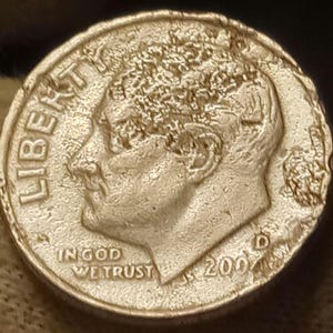 May include: A close-up of a United States dime coin. The coin features a profile of a person, the word "LIBERTY", and the phrase "IN GOD WE TRUST". The year "2000" is visible.
