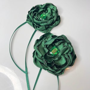 以下が含まれることがあります： 緑色の宝石が中央に付いた、濃い緑色の布製のフラワーブローチが2つ