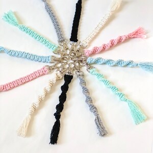 May include: A collection of colorful crocheted keychains with tassels, featuring a variety of colors including black, white, gray, pink, light blue, and mint green. The keychains are attached to silver key rings.