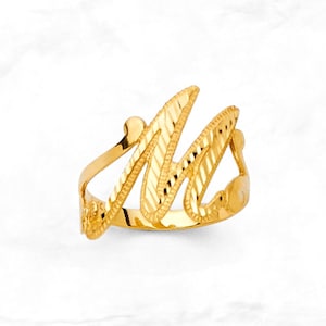 May include: A gold-coloured ring shaped like the letter "M". The ring features a textured pattern on the letter and band. The ring is set against a white background.