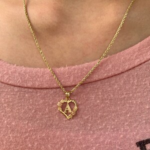 May include: A gold chain necklace with a heart-shaped pendant featuring the letter "A" surrounded by small floral details.