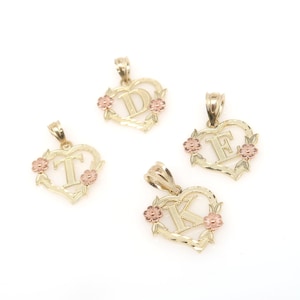 May include: Three gold heart-shaped pendants with different letters, D, E, and K, in the center. Each pendant has a floral design around the letter and pink accents.