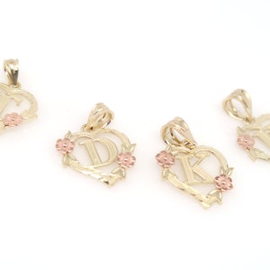May include: Four gold heart-shaped pendants with different letters in the center. Each pendant has a floral design around the letter and two small pink flowers on the sides.