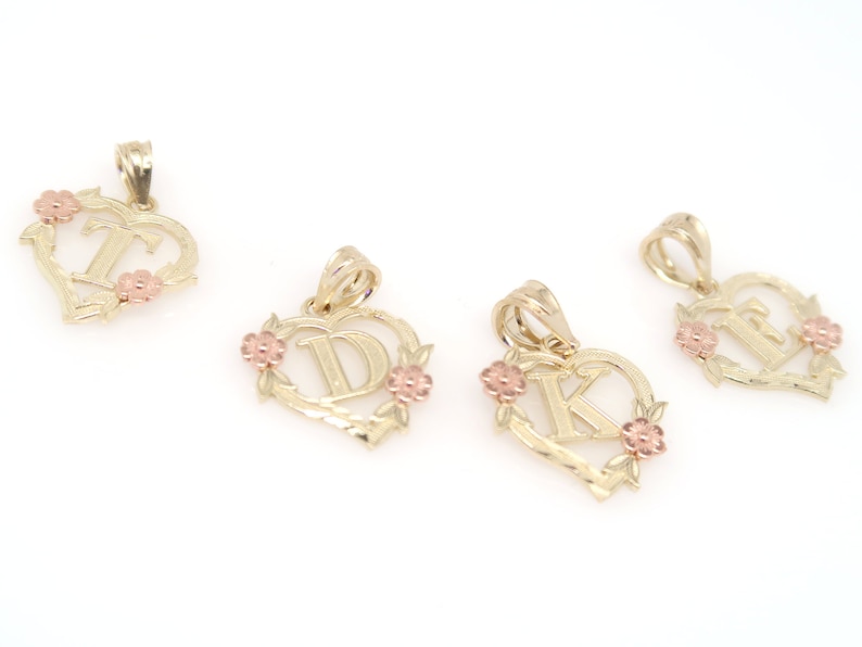 May include: Four gold heart-shaped pendants with different letters in the center. Each pendant has a floral design around the letter and two small pink flowers on the sides.