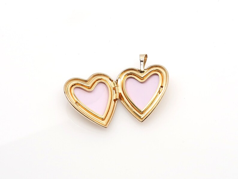 May include: A gold heart-shaped locket pendant with a pink interior. The locket is open, revealing the two halves of the heart.