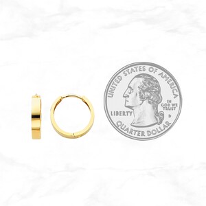 May include: Two gold-colored hoop earrings with a flat, rectangular design. The earrings are shown next to a U.S. quarter for size comparison. The earrings have a simple, modern style and a polished finish.