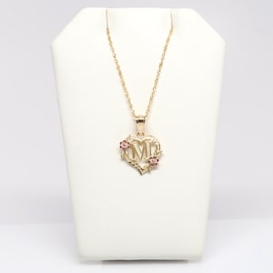 May include: A gold necklace with a heart-shaped pendant featuring the letter "M" surrounded by small pink flowers.