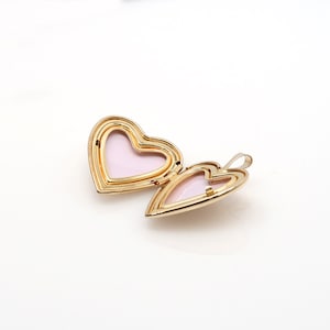 May include: A gold heart-shaped locket with a pink interior. The locket is open and the hinge is visible.