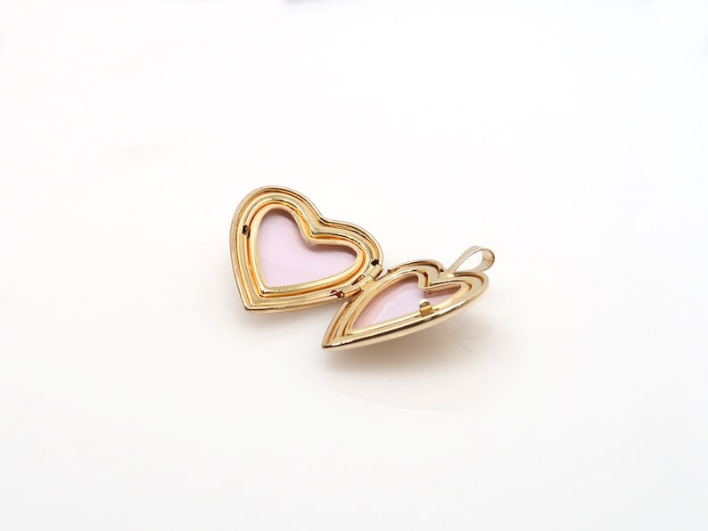 May include: A gold heart-shaped locket with a pink interior. The locket is open and the hinge is visible.