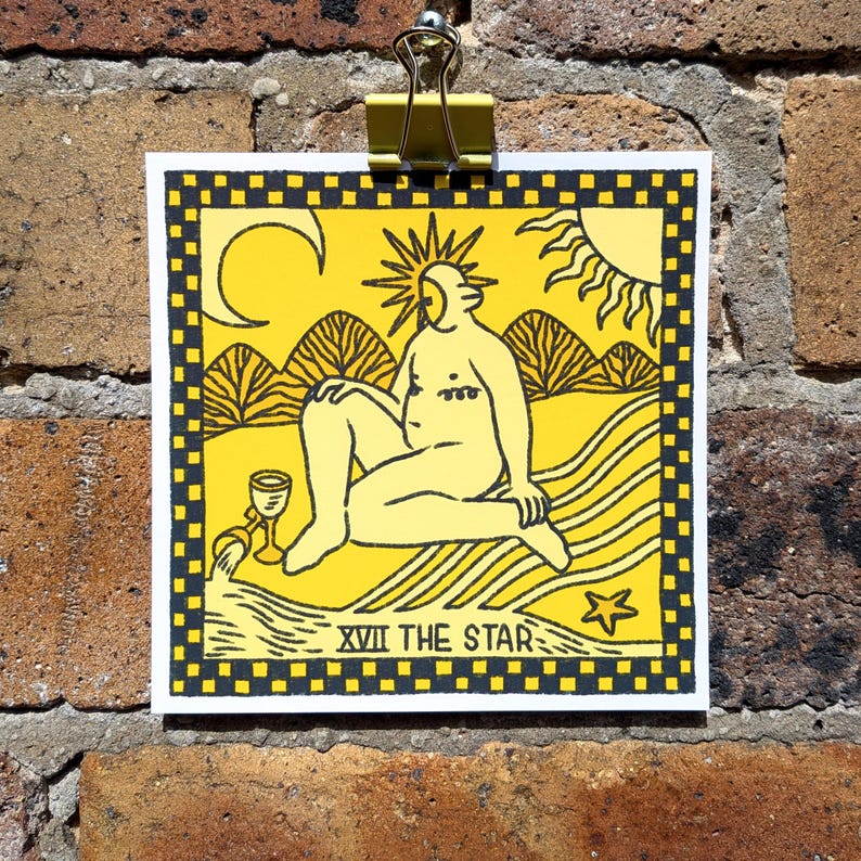 Op de afbeelding: Een vierkante print met een gele en zwarte illustratie van een figuur die bij een beekje zit onder een zon en maansikkel. Het ontwerp bevat een kelk, een ster en de tekst XVII THE STAR, alles binnen een zwart-gele geblokte rand.