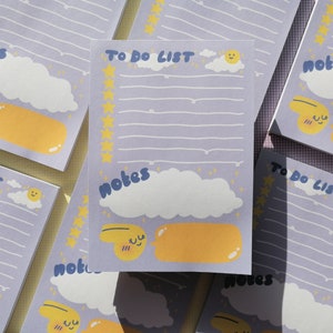 May include: A rectangular notepad with a light purple background featuring the text TO DO LIST and notes. The design includes white clouds, a yellow sun, a column of yellow stars, and a yellow speech bubble graphic with a smiling face character.