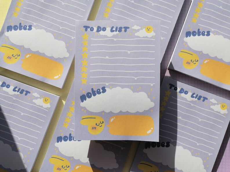 May include: A rectangular notepad with a light purple background featuring the text TO DO LIST and notes. The design includes white clouds, a yellow sun, a column of yellow stars, and a yellow speech bubble graphic with a smiling face character.
