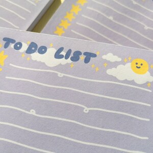 May include: A light purple notepad with the text TO DO LIST in dark blue. The page features white horizontal lines, a vertical column of yellow stars on the left, and a graphic of a smiling yellow sun with white clouds and small yellow stars.