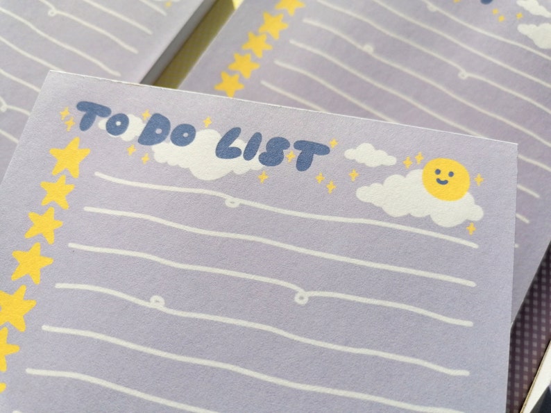 May include: A light purple notepad with the text TO DO LIST in dark blue. The page features white horizontal lines, a vertical column of yellow stars on the left, and a graphic of a smiling yellow sun with white clouds and small yellow stars.