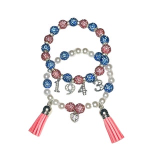 May include: Two bracelets with pink and blue beads, a white pearl bracelet with a heart charm and a charm with the number 1943. The bracelets have pink tassels.