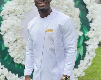 May include: A white textured long-sleeve shirt and matching pants. The shirt has a gold accent on the chest and gold buttons on the sleeves. The person is wearing a gold watch and sunglasses.