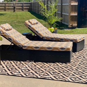 Puede incluir: Dos tumbonas de mimbre negro con cojines de estampado beige y blanco. Las tumbonas est&aacute;n sobre una alfombra geom&eacute;trica de exterior en blanco y negro.