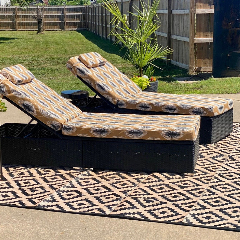 Puede incluir: Dos tumbonas de mimbre negro con cojines de estampado beige y blanco. Las tumbonas est&aacute;n sobre una alfombra geom&eacute;trica de exterior en blanco y negro.