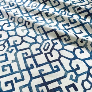 May include: Close-up of a white fabric with a repeating geometric pattern in shades of blue. The design features interlocking shapes and lines, creating a textured appearance. The fabric is slightly wrinkled, adding depth to the design. Ideal for home decor or fashion.