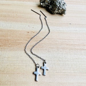 May include: A pair of silver cross dangle earrings with a chain and a small silver bar at the top.