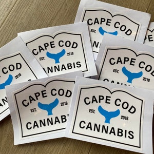 May include: A collection of white stickers with a black border and the words "CAPE COD CANNABIS" in black text. The stickers feature a blue whale tail design and the text "EST. 2018".