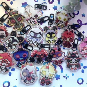 May include: A collection of 15 colorful character keychains with black metal clasps. The keychains feature various cartoon characters with different expressions and poses. The characters are all wearing different outfits and accessories.