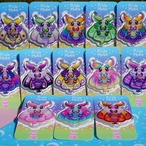Puede incluir: Doce pines de polilla arcoíris del orgullo en tarjetas blancas con el texto "Pride Moth" en cada tarjeta. Las polillas son de diferentes colores y tienen un diseño arcoíris.