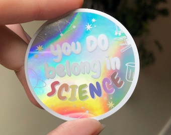 Może przedstawiać: Okrągła, holograficzna naklejka z napisem "you DO belong in SCIENCE" w tęczowym wzorze. Naklejka ma białą obwódkę i małe ilustracje związane z nauką.