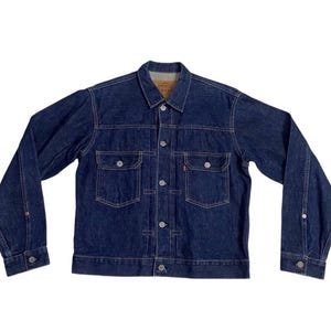 Op de afbeelding: Een witte keramische mok met een zwart handvat en de tekst "But First, Coffee" in een zwarte, handgeschreven lettertype. De mok staat op een wit oppervlak.