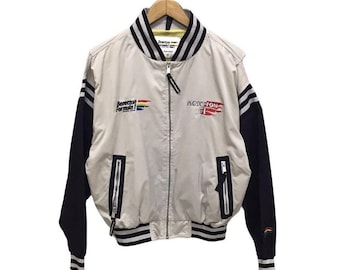 May include: A white bomber jacket with black sleeves and a rainbow stripe on the left side. The jacket has a zipper closure and two pockets on the front. The text "Benetton Formula 1" is printed on the jacket.
