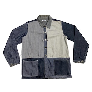 Puede incluir: Una chaqueta vaquera azul con un diseño de patchwork. La chaqueta tiene un cierre de botones, mangas largas y dos bolsillos en la parte delantera. La tela es una mezcla de denim azul sólido y denim a rayas.